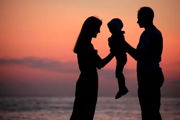 Silhouettes of parents with child on hands against sea decline — Stock Photo, Image