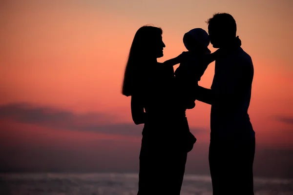 Las siluetas de los padres con el niño en las manos contra el declive del mar —  Fotos de Stock