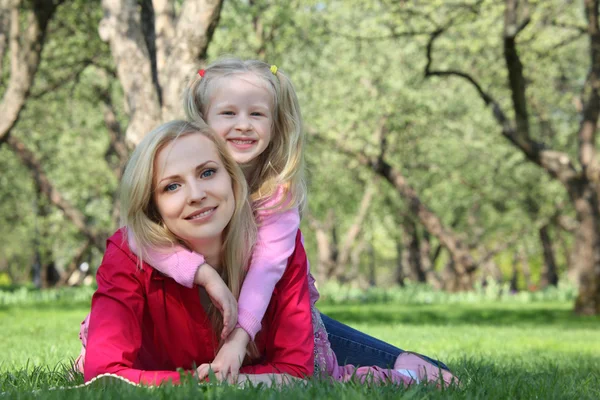 Daughter embraces behind mother lying on grass in park — Stock Photo, Image