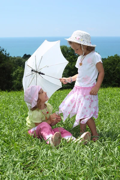 用一把雨伞在草坪上的两个小女孩 — 图库照片