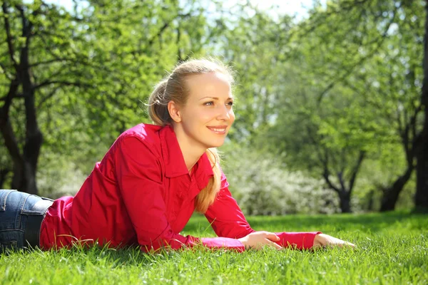 Krásná blondýnka leží na trávě v zahradě na jaře — Stock fotografie