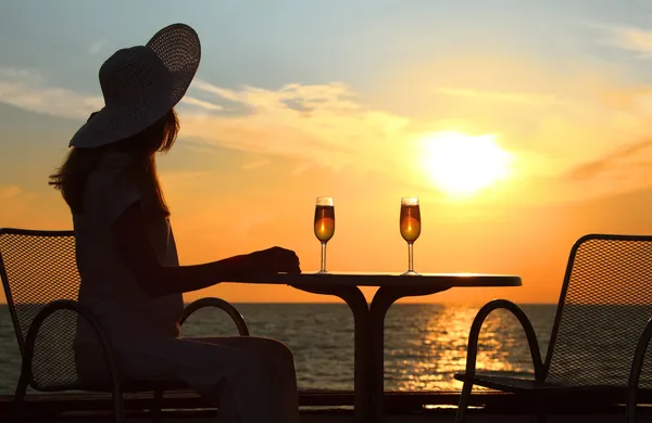 Weibliche Silhouette bei Sonnenuntergang hinter Tisch mit zwei Gläsern — Stockfoto