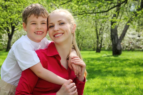 Son embraces behind mother in park in spring — Stock Photo, Image