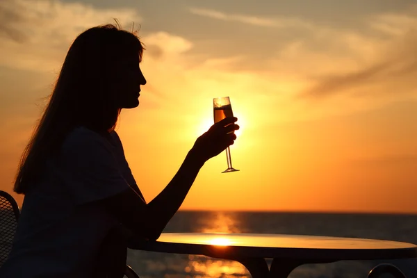 Vrouwelijke silhouet op zonsondergang aan tafel met glas in hand — Stockfoto