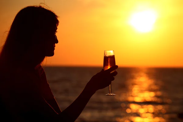 Silueta femenina en la puesta de sol del mar con vidrio en la mano — Foto de Stock