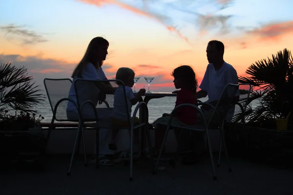 Rodzina przy stole na plaży przy zachodzie słońca — Zdjęcie stockowe