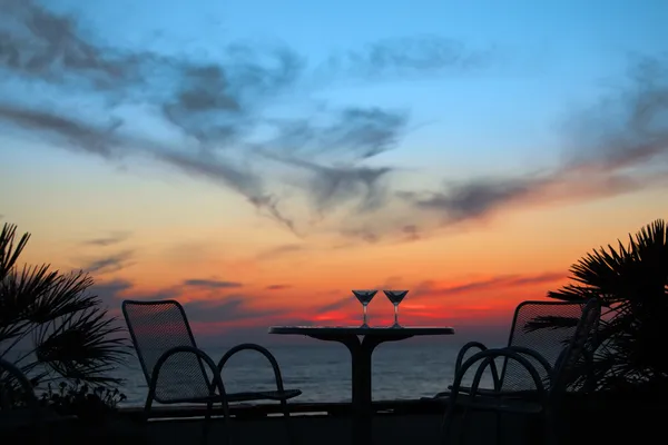 Mesa com dois copos de vinho ao pôr do sol no mar ao ar livre — Fotografia de Stock