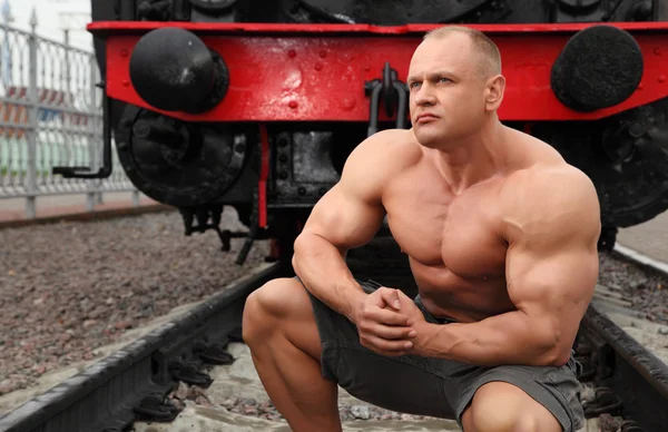 Strong shirtless man sits on railroad against locomotive — Stock Photo, Image