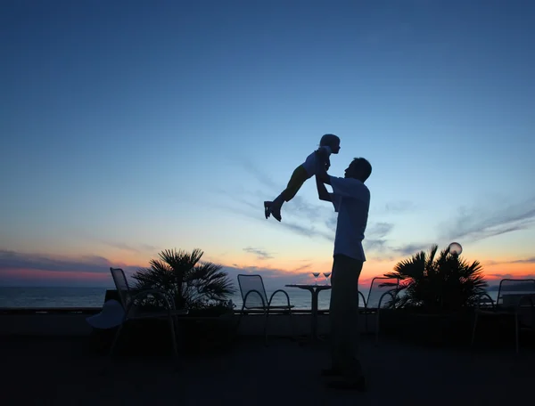 Silhuett av mann med barn i hendene ved solnedgang – stockfoto