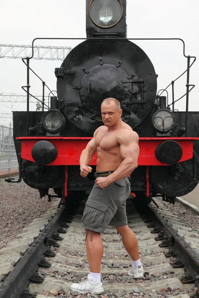Ισχυρός άνδρας shirtless στέκεται επάνω σιδηρόδρομος κατά ατμομηχανή — Φωτογραφία Αρχείου