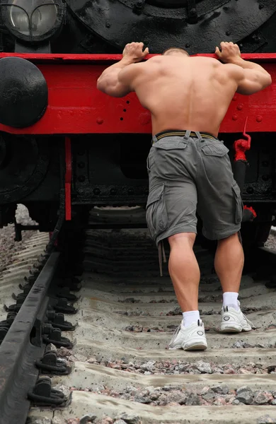 Сильний без сорочки чоловік штовхає локомотив — стокове фото