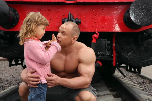 Homem sem camisa forte senta-se na estrada de ferro com a menina — Fotografia de Stock