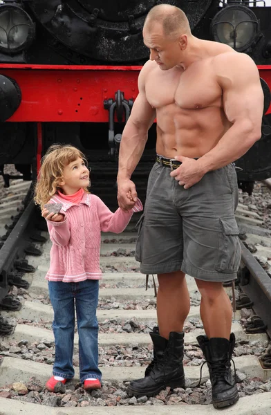 Homem sem camisa forte fica na estrada de ferro com a menina — Fotografia de Stock