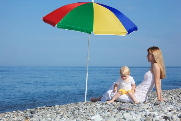 Mãe com criança sob um guarda-chuva multi colorido na praia de seixos — Fotografia de Stock