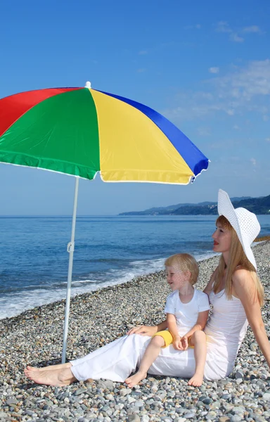 Matka z dzieckiem pod multi kolorowy parasol na kamienistej plaży — Zdjęcie stockowe