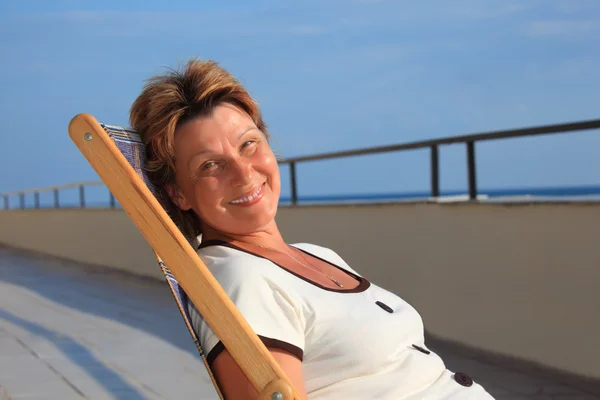 Middleaged woman in lounge on veranda over sea — Stock Photo, Image
