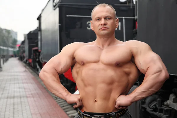 Athlete shows muscles against train — Stock Photo, Image