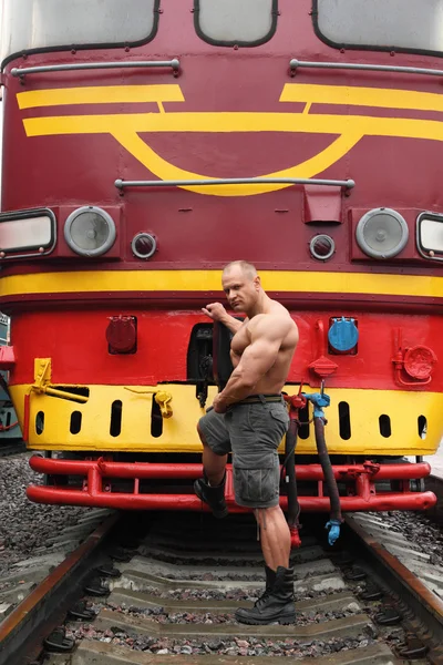 Shirtless sportovec stojí na železnici proti lokomotiva — Stock fotografie