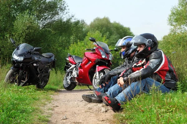 Two motorcyclists sitting on country road near bikes — Stock Photo, Image