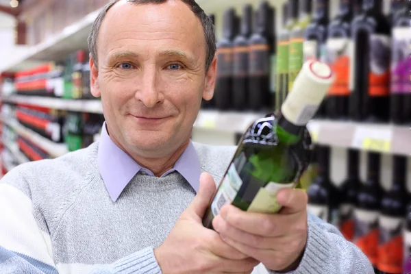 Homem idoso feliz na loja com garrafa de vinho nas mãos — Fotografia de Stock