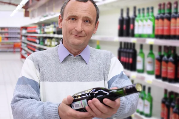 Glad äldre man i butik med vinflaska i händer — Stockfoto