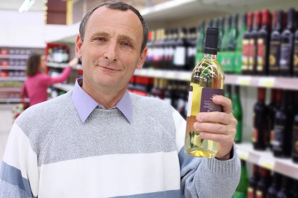 Elderly man in shop holds wine bottle in hand — Stock Photo, Image