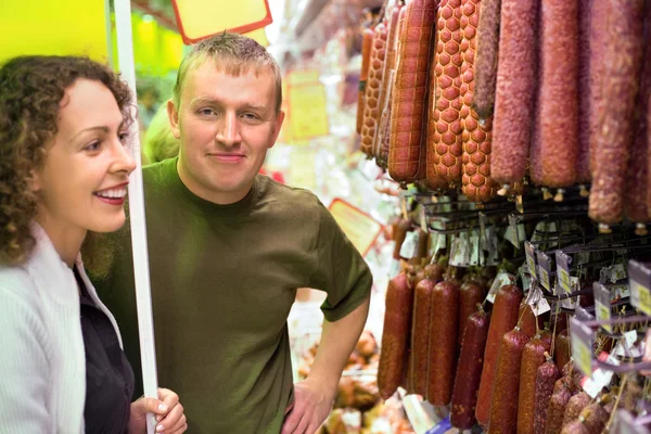Улыбающиеся юноша и девушка покупают колбасу в супермаркете — стоковое фото