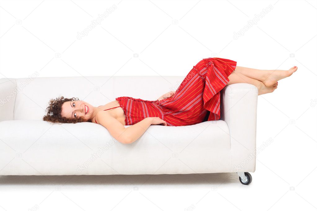 Young beautiful barefooted woman in red dress lies on white leat