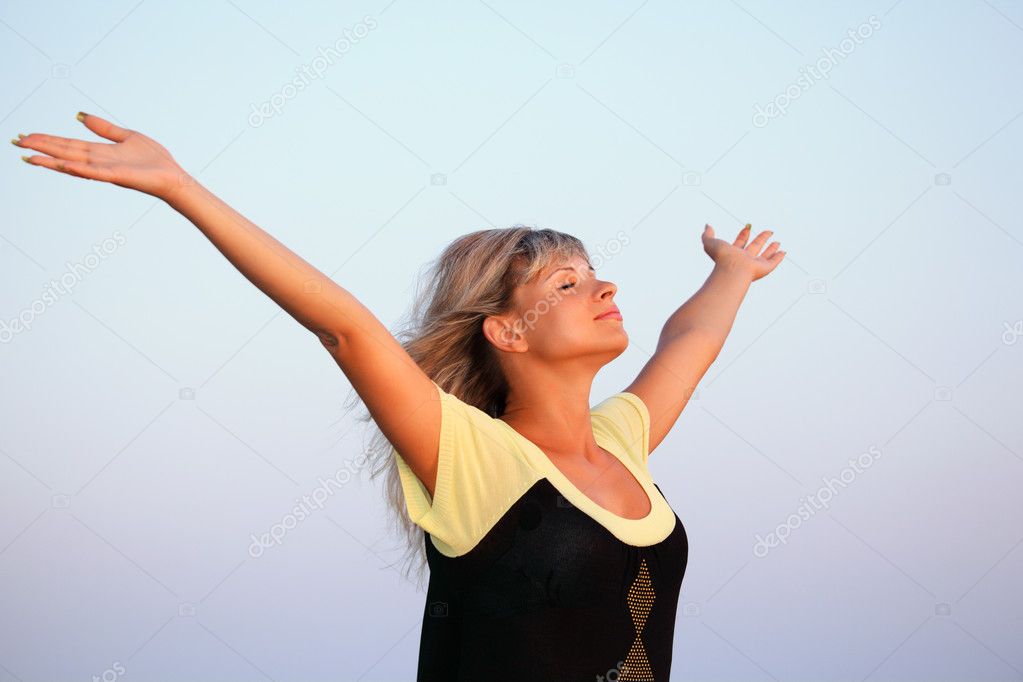 Beautiful young woman lifted hands upwards against sky