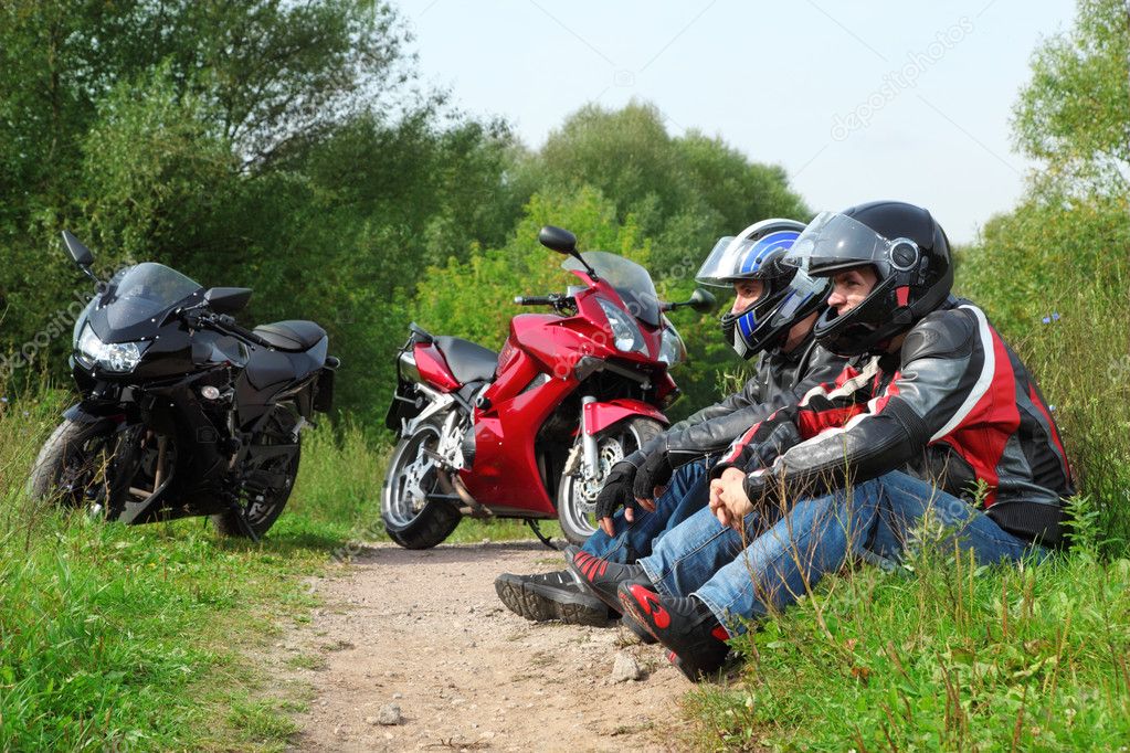 Two motorcyclists sitting on country road near bikes