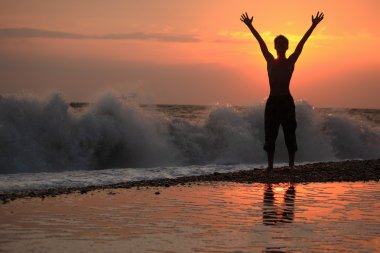 Silhouette guy lifted hands upwards on sunset wavy beach clipart