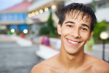 Smiling teenager boy standing near hotel on resort in evening clipart