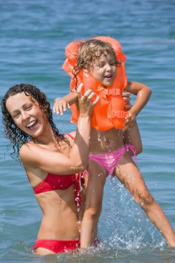 Young woman keeps in hands little girl in lifejackets in sea on clipart