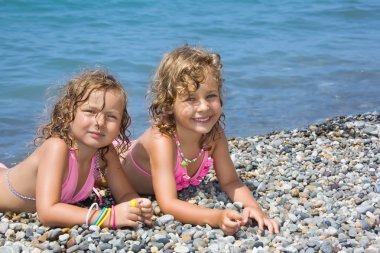 Two pretty little girls lying on stony beach near sea clipart