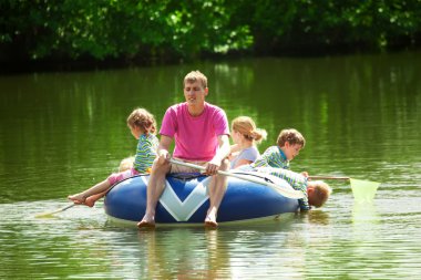 Children and adults float on an inflatable boat in a sunny day clipart