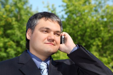 Businessman speaking by phone outdoor in summer clipart