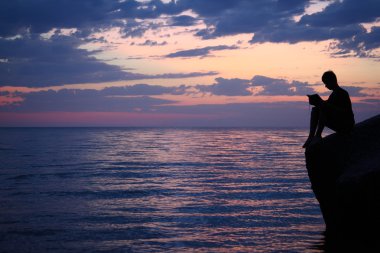 Silhouette guy sitting on breakwater in evening near sea, reads clipart