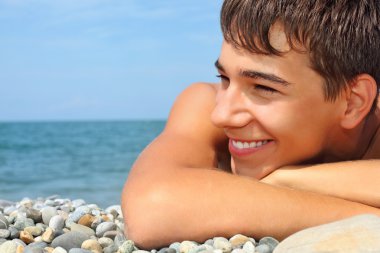 Teenager boy lying on stony seacoast, looking afar clipart