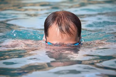 Young man in watersport goggles swimming in pool, dives under wa clipart