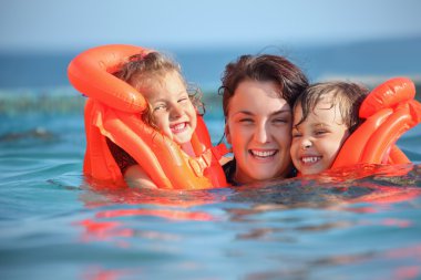 Two little girls bathing in lifejackets with young woman in pool clipart