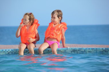 Two little girls in lifejackets sitting on ledge pool on resort, clipart