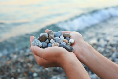 Handful of stones in hands, Against stones and sea clipart