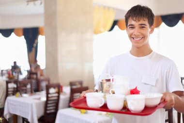 genç gülümseyen nazik garson tepsi yemekleri restauran tutar.