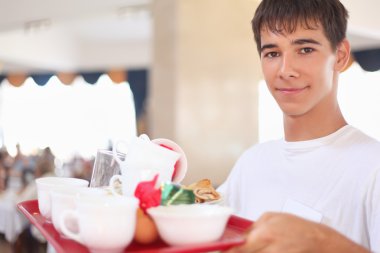 Young smiling affable waiter keeps tray with dishes at restauran clipart