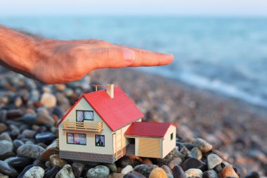 Model of house with garage on stony beach in evening, Man's hand clipart