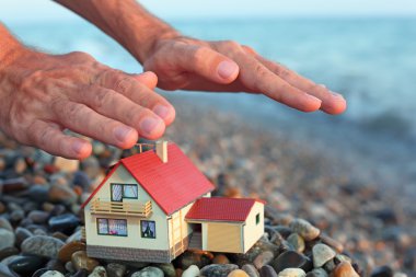 Model of house with garage on stony beach in evening, Man's hand clipart