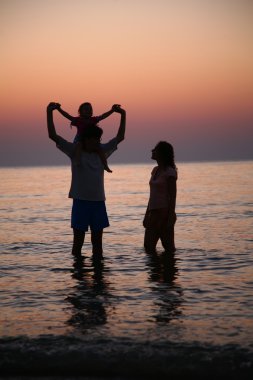 Family in sea alongshore on sunset clipart