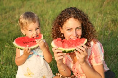 Mother and daughter eat watermelon on the grass clipart