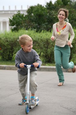 Mother runs after the son on the bicycle clipart