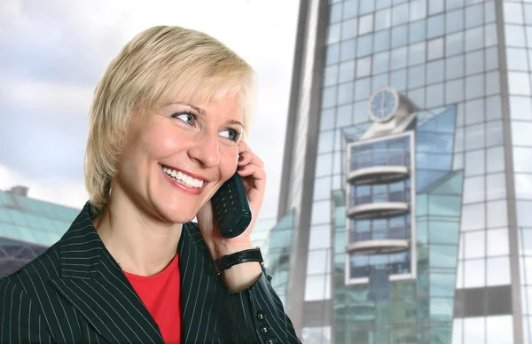 Blonde vrouw met telefoon in de buurt van moderne glazen gebouw — Stockfoto
